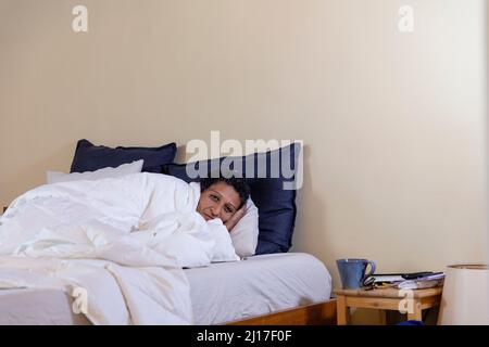Frau, die zu Hause auf dem Bett mit weißer Decke liegt Stockfoto