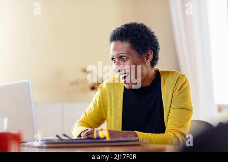 Überraschte Geschäftsfrau mit Laptop zu Hause Stockfoto