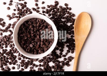 Blick von oben auf frische Schokoladenstückchen mit Schale und Holzlöffel auf weißem Hintergrund Stockfoto