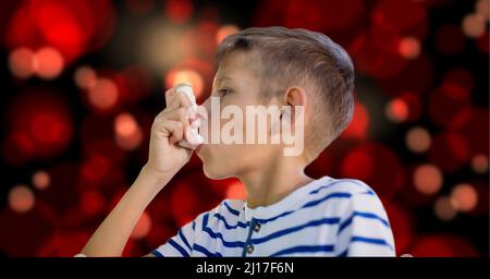 Kaukasischer Junge mit einem Asthma-Inhalator gegen rote Lichtflecken auf schwarzem Hintergrund Stockfoto