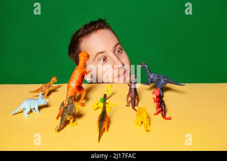 Junger Mann mit Dinosaurierfiguren vor grünem Hintergrund Stockfoto