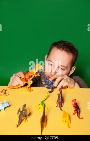 Junger Mann spielt mit Dinosaurierfiguren vor grünem Hintergrund Stockfoto