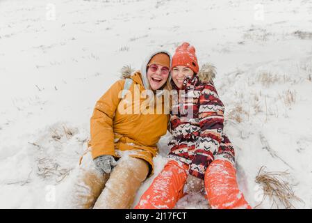 Fröhliche Frauen in warmer Kleidung, die im Schnee sitzen Stockfoto