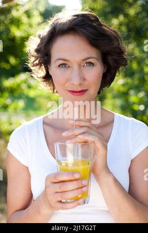 Frau im Park mit einem Glas frischen Orangensaft Stockfoto