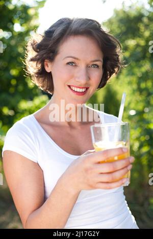 Glückliche Frau mit Orangensaft, der neben Bäumen steht Stockfoto