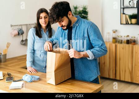 Mann, der in einer Papiertüte bei einer Frau in der Küche zu Hause steht Stockfoto