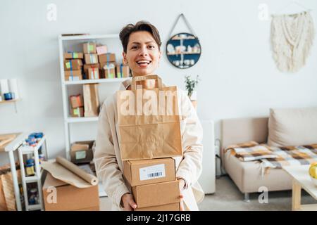 Fröhliche Handwerkerin, die Pakete in der Werkstatt trägt Stockfoto