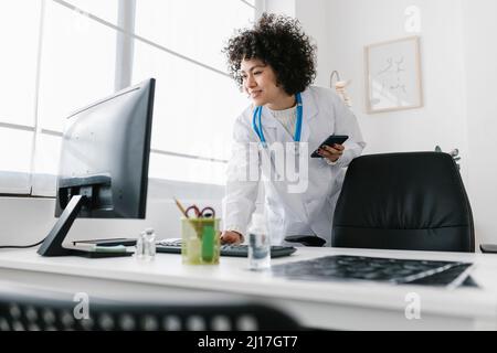 Arzt mit Smartphone am Computer in der Klinik Stockfoto