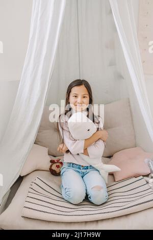Glückliches Mädchen mit Spielzeug sitzt auf dem Bett zu Hause Stockfoto