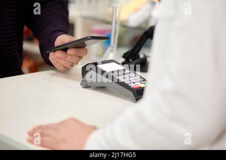 Der Kunde, der kontaktlos über das Smartphone am Kassenschalter im Geschäft bezahlt Stockfoto