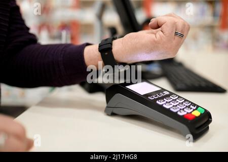 Mann, der kontaktlos über eine Smart Watch am Kassenschalter im Geschäft bezahlt Stockfoto