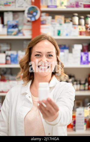 Glücklicher Apotheker, der eine Flasche Medizin im Apothekenladen gibt Stockfoto