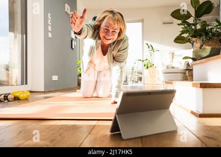 Lächelnde ältere Frau macht Übung beobachten Online-Tutorial durch Tablet-PC zu Hause Stockfoto