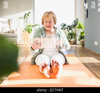 Glückliche ältere Frau mit Trinkglas mit digitalem Tablet-PC zu Hause Stockfoto