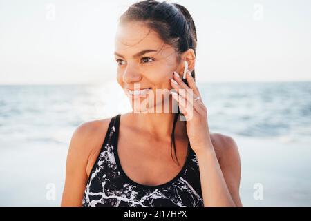 Lächelnde, schöne Frau, die an sonnigen Tagen kabellose in-Ear-Kopfhörer trägt Stockfoto