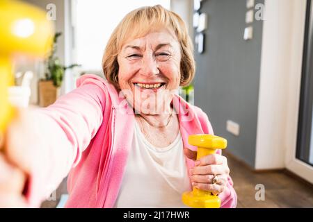 Fröhliche ältere Frau, die zu Hause mit gelben Hanteln ausarbeitet Stockfoto
