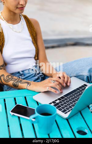 Junge Frau mit Tätowierung auf Laptop sitzend am Tisch Stockfoto