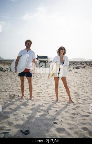 Glückliches Paar, das mit Surfbrett am Strand steht Stockfoto