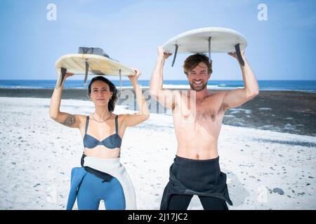 Ein glückliches Paar, das an einem sonnigen Tag Surfbrett am Strand trug Stockfoto