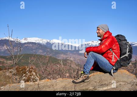 Lächelnder Mann mit Rucksack auf Felsen sitzend Stockfoto