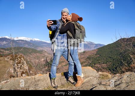 Frau küsst Freund nehmen Selfie durch Smartphone an sonnigen Tag Stockfoto