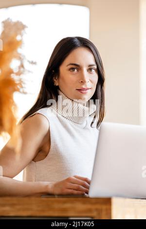 Selbstbewusste Geschäftsfrau mit Laptop, die zu Hause arbeitet Stockfoto