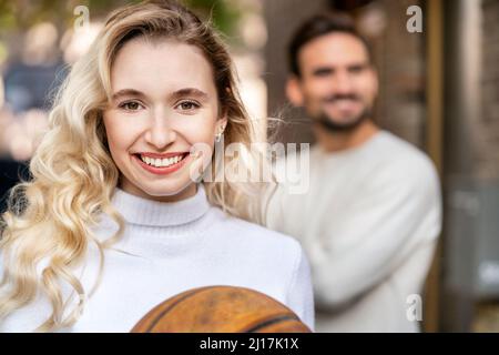 Glückliche blonde Frau mit Basketball vor dem Freund stehen Stockfoto