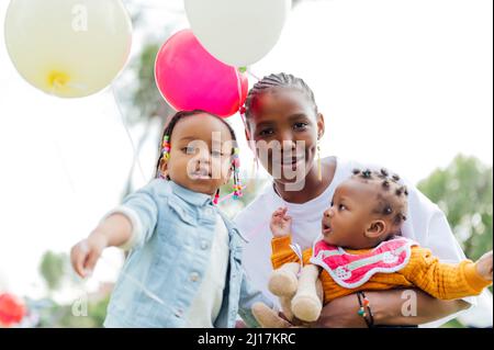 Lächelnde Mutter mit Töchtern, die Luftballons im Park halten Stockfoto