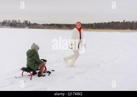 Frau, die den Sohn auf der Rodel sieht und im Winter genießt Stockfoto