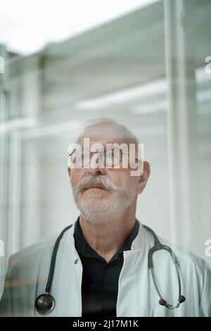 Nachdenklicher Arzt mit Schnurrbart und Brillen in der medizinischen Klinik Stockfoto