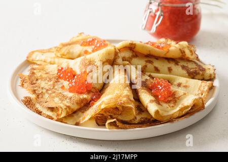 Dünne Pfannkuchen mit rotem Kaviar auf weißem Hintergrund. Traditionelles russisches Frühstück für Fasching. Stockfoto