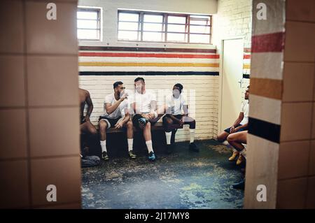 Der Gewinner sitzt hier. In voller Länge eine Gruppe hübscher junger Rugby-Spieler, die sich unterhalten, während sie in einer Umkleidekabine sitzen. Stockfoto