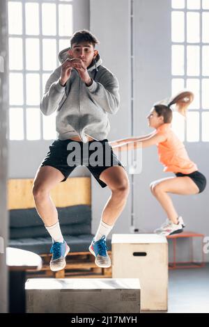 Junger Mann mit Frau, die im Fitnessstudio Jumping Squats auf einer Holzkiste macht Stockfoto