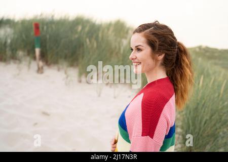 Lächelnde rothaarige junge Frau, die bei der Wiese steht Stockfoto