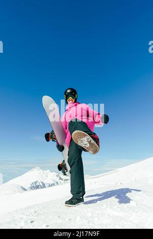 Mann mit Snowboard-Treten, der auf verschneiten Bergen steht Stockfoto