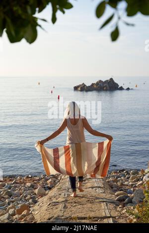 Frau mit Decke, die an sonnigen Tagen am Strand spazieren ging Stockfoto