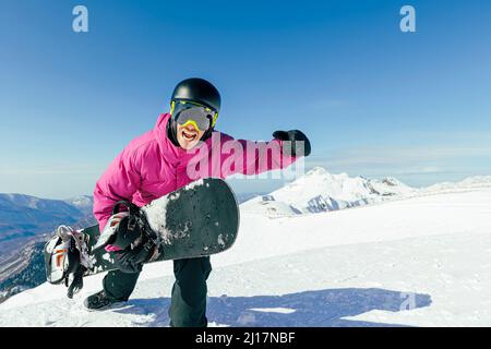 Mann mit Snowboard, der am sonnigen Tag auf dem verschneiten Berg schreit Stockfoto