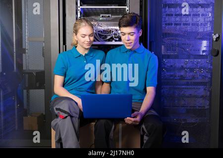 Techniker mit Laptop sitzen im Serverraum der Industrie Stockfoto