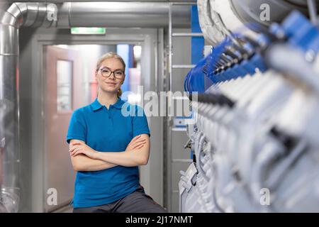 Glücklicher Techniker, der mit gekreuzten Armen im Werk steht Stockfoto