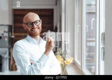 Glücklicher kahler Mann, der im Büro eine Brille trägt und gestikiert Stockfoto