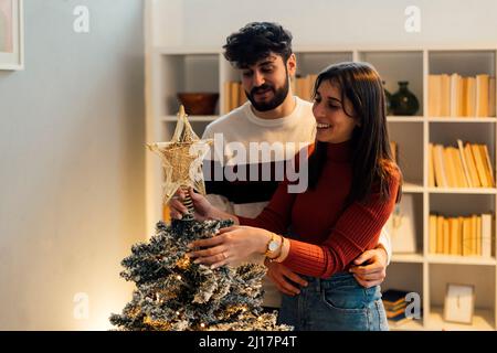 Glückliches Paar dekorieren und Stern auf Weihnachtsbaum zu Hause setzen Stockfoto