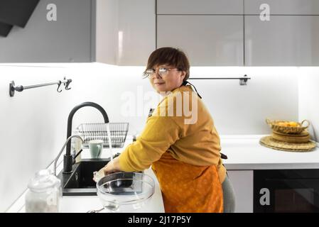 Ältere Frau, die zu Hause in der Küche Geschirr wäscht Stockfoto