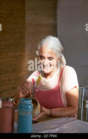 Lächelnder Künstler malt Tontopf auf einem Stuhl Stockfoto