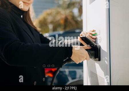 Junge Frau, die das Ladegerät an der Ladestation ansteckt Stockfoto