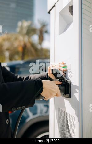 Frau, die das Ladegerät für Elektroautos an der Ladestation ansteckt Stockfoto