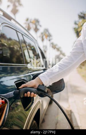 Hand eines Mannes, der den Ladestecker des Elektroautos am Straßenrand hält Stockfoto