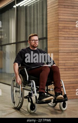 Geschäftsmann, der auf einem Rollstuhl im Büroflur sitzt Stockfoto