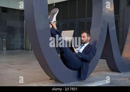 Geschäftsmann mit Laptop, der auf einer Architekturfunktion auf dem Fußweg liegt Stockfoto