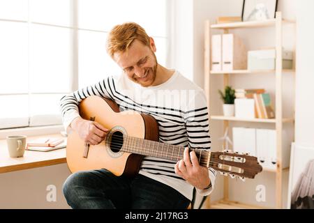 Glücklicher junger Mann, der zu Hause Gitarre spielt Stockfoto