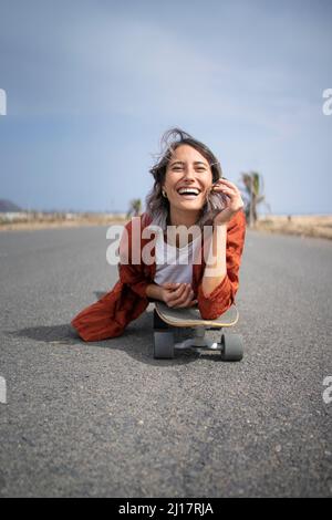 Glückliche junge schöne Frau, die auf der Straße über dem Skateboard liegt Stockfoto
